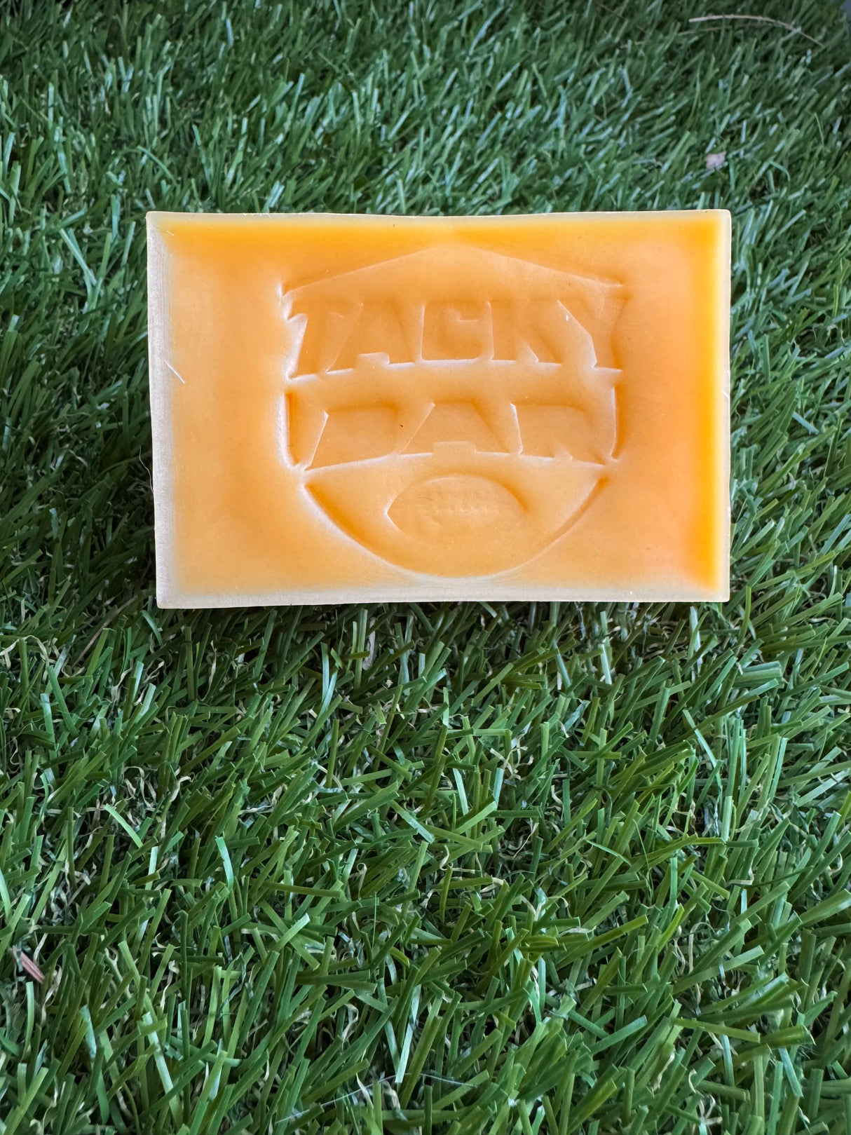 A rectangular yellow bar of soap with an embossed design on it, placed on a grass-like surface.
