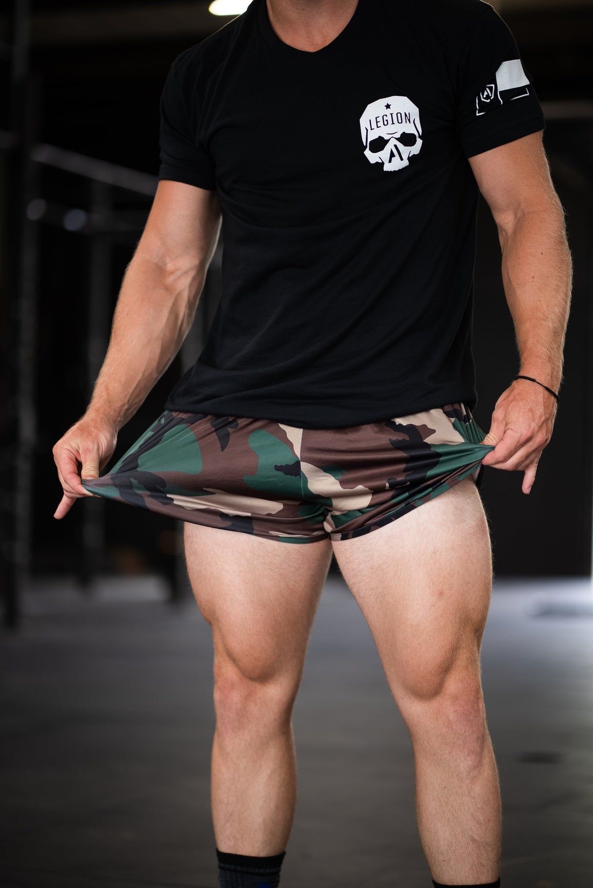 Person wearing a black t-shirt with a logo and camouflage shorts.