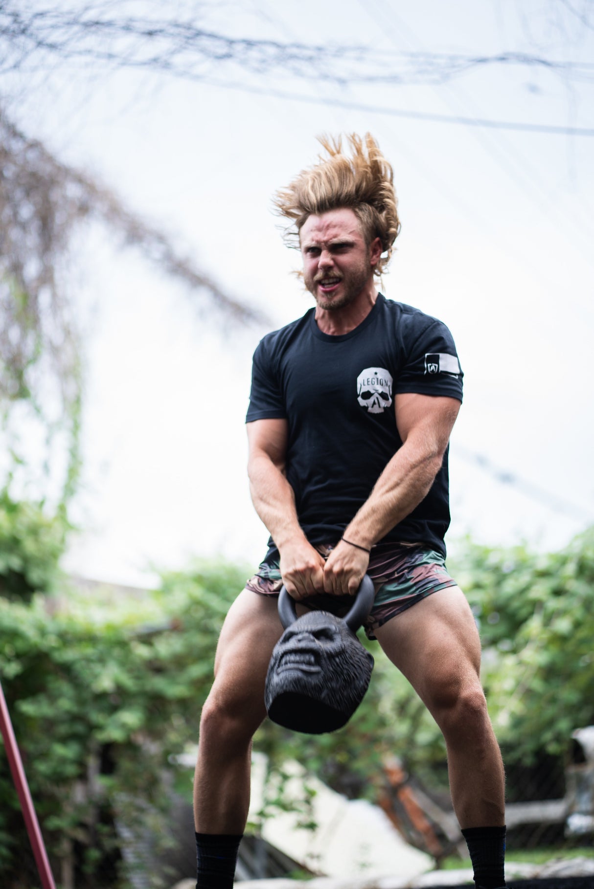 Man lifting a kettlebell outdoors with trees in the background