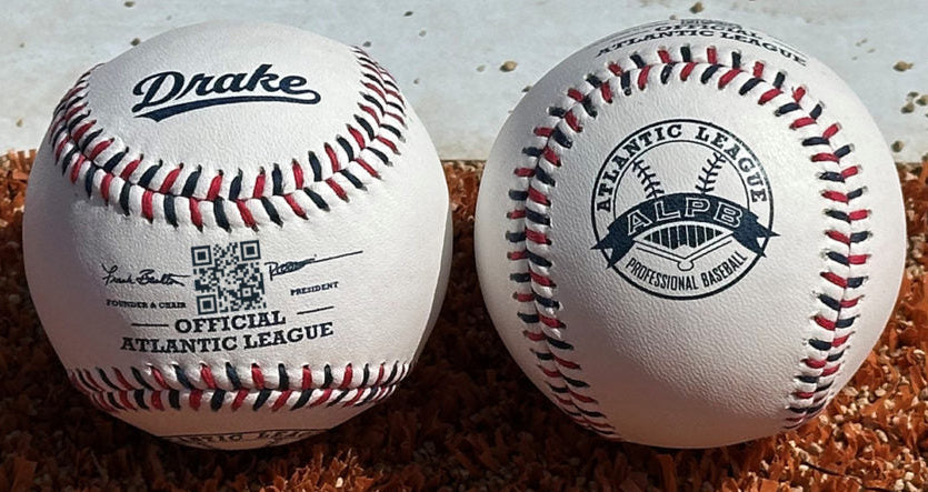 Two baseballs resting on reddish-brown sand or dirt, one white with a black Drake logo and the other white with an Atlantic League ALPS professional baseball logo.