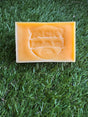 A rectangular yellow bar of soap with an embossed design on it, placed on a grass-like surface.