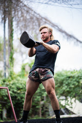 Man lifting a kettlebell outdoors with greenery in the background
