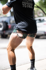 Person wearing a black t-shirt with text and camouflage shorts on a street.