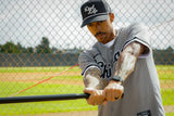 Man in a baseball uniform with 'Dad Life' cap holding a bat on a baseball field.