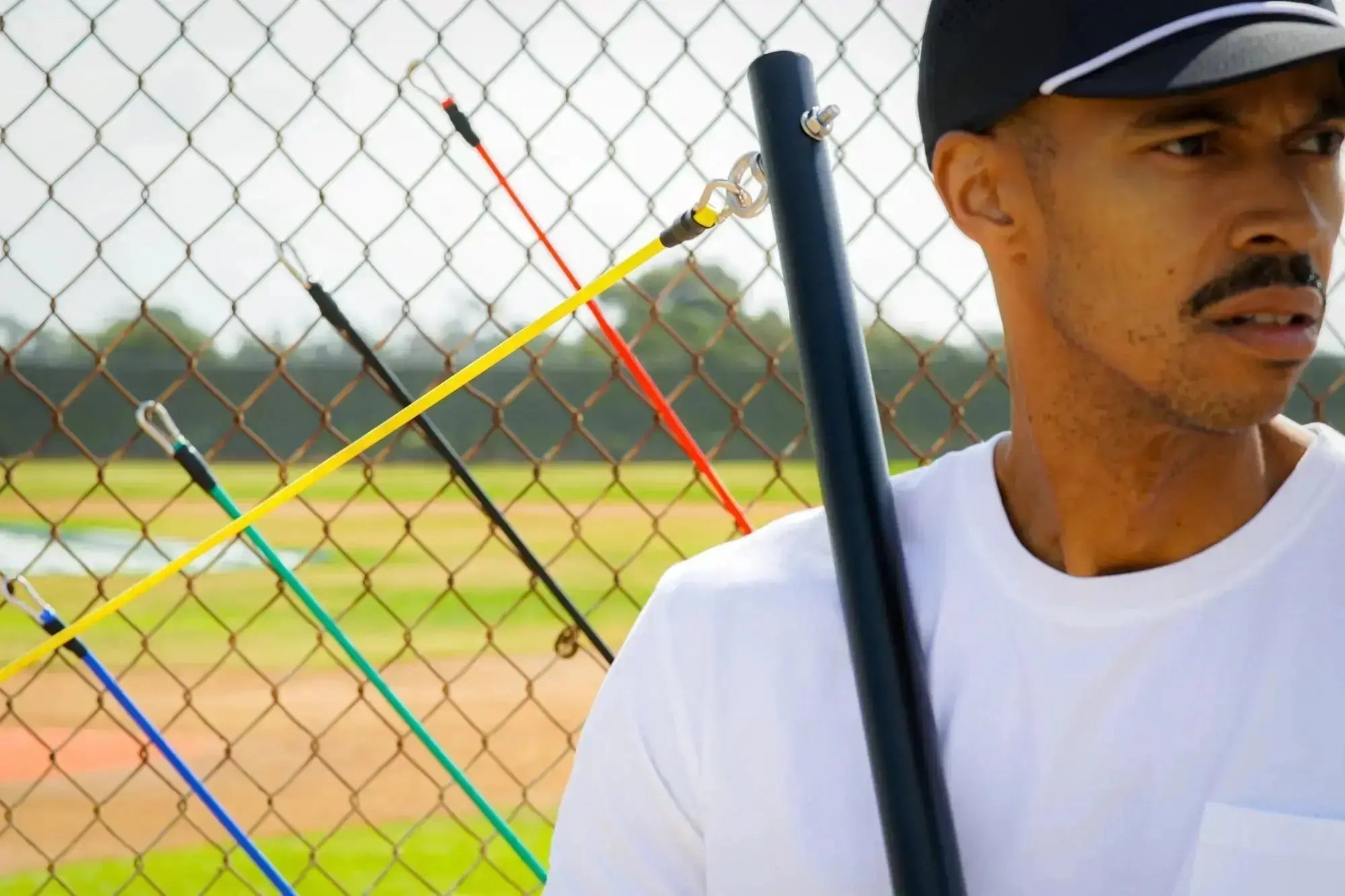 Man holding a baseball bat with a chain-link fence and field in the background