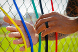Hands holding colorful sticks against a chain-link fence background