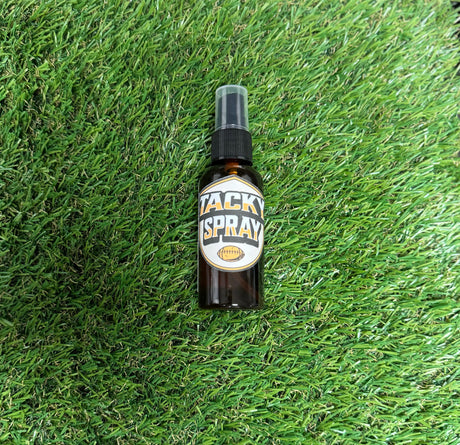 A bottle of Tacky Sray placed on green grass, with a label that includes the product name and branding.