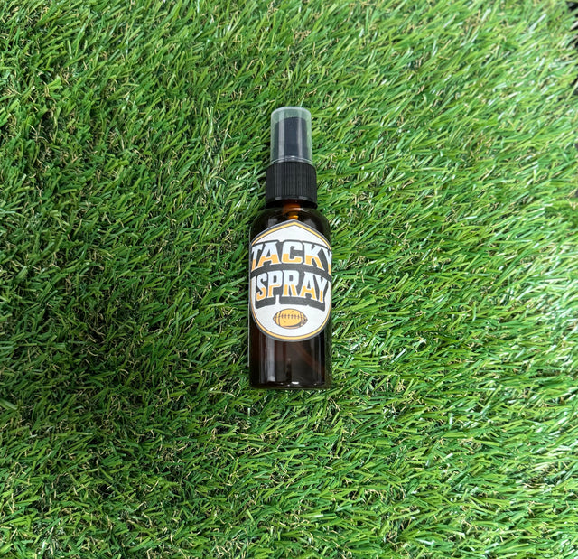 A bottle of Tacky Sray placed on green grass, with a label that includes the product name and branding.