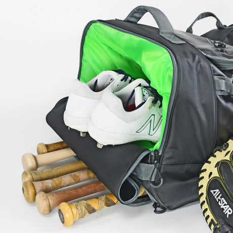 Gray sports bag with green interior, containing white cleats and baseball bats, on a light gray background.