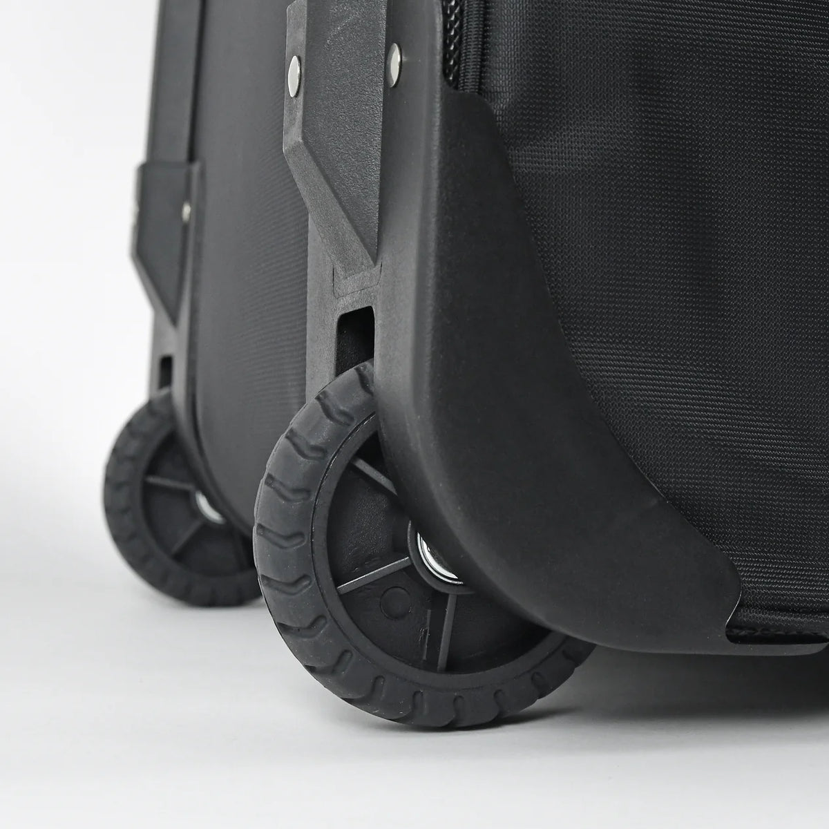 Close-up of a black hard-shell rolling suitcase showing the front wheel, protective wheel cover, and textured fabric side panel on a light gray background.