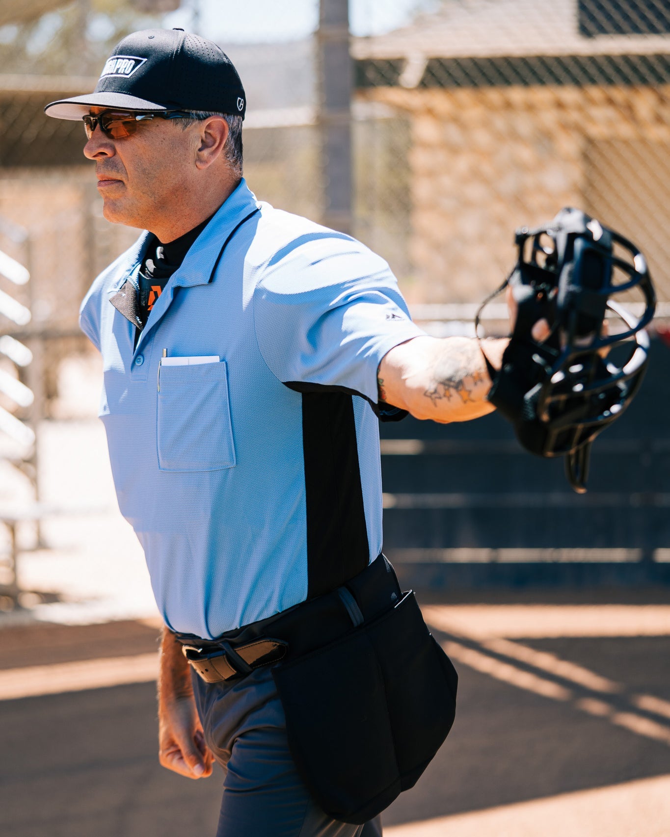 Man in a blue shirt and black cap holding a baseball glove on a sports field.
